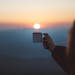 A person holds a coffee cup against a beautiful sunrise, capturing a serene outdoor moment.
