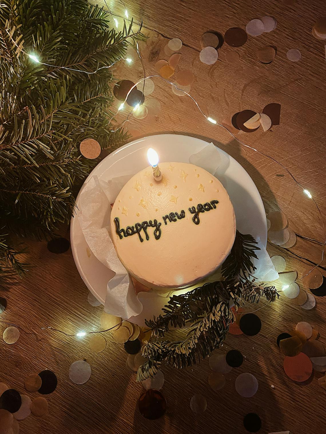 A New Year celebration cake with candle, decorations, and confetti in a cozy setting.