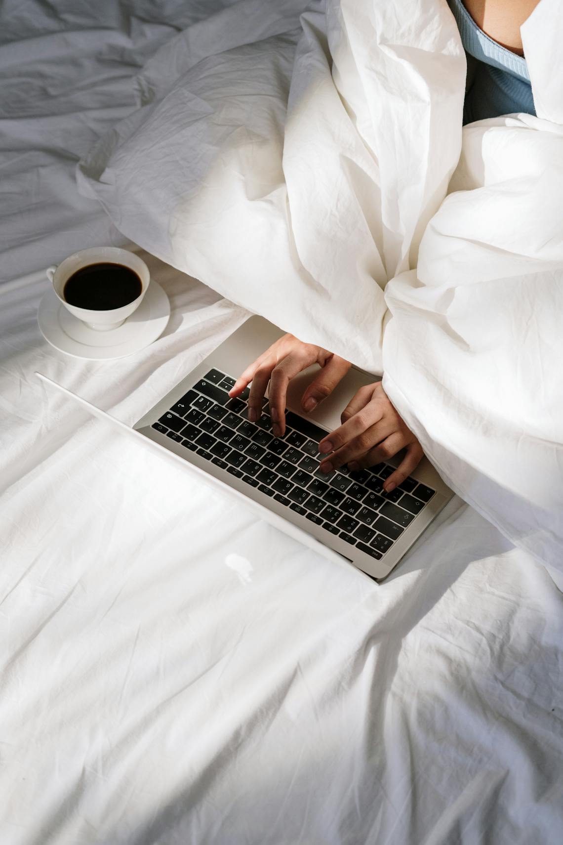 Comfortable home office setup with a laptop on bed and a cup of coffee, perfect for remote work.