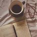 Flat lay of coffee, open notebook, pen, and eyeglasses on a fabric surface.
